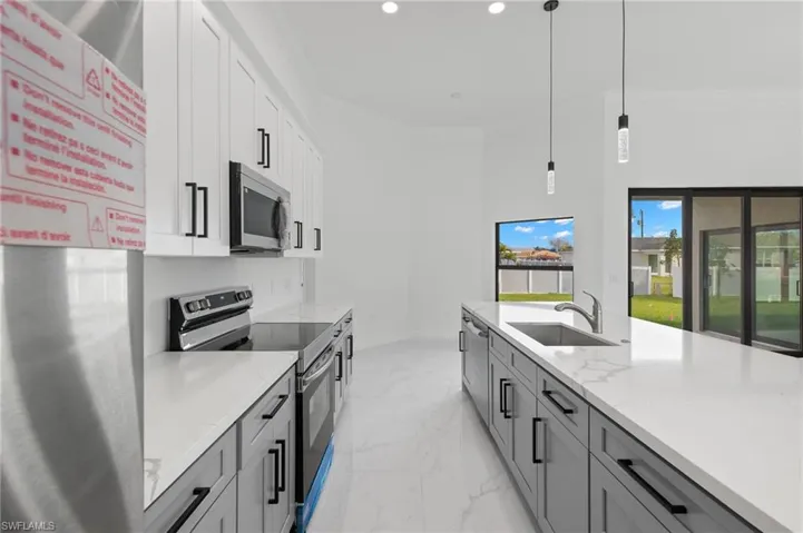 Dual tone kitchen with stainless steel appliances, pendant lighting, ornamental molding, light stone countertops, and light marble finish floors