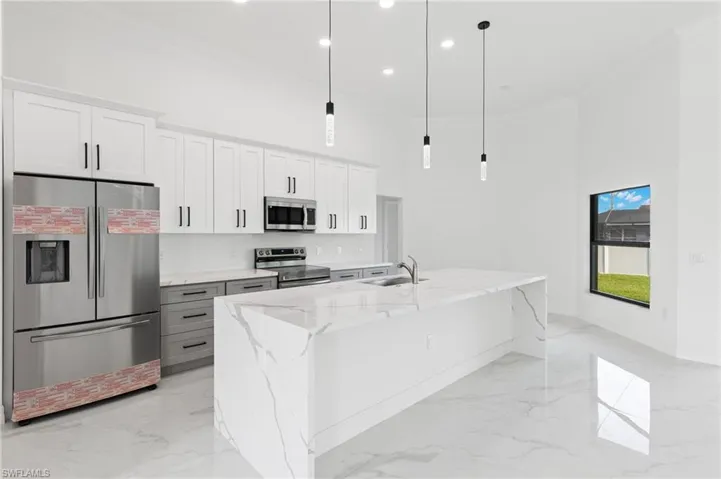 Kitchen with stainless steel appliances, light stone counters, white cabinetry, decorative light fixtures, and a high ceiling