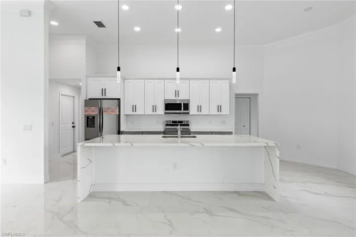 Kitchen with light stone counters, stainless steel appliances, white cabinets, ornamental molding, and a spacious island