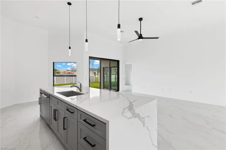 Kitchen with pendant lighting, ornamental molding, a center island with sink, gray cabinets, and open floor plan