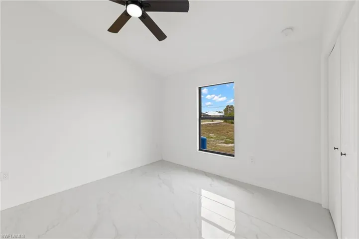 Spare room featuring lofted ceiling, marble look tiles, and ceiling fan