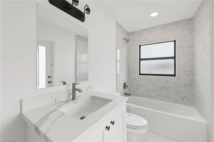 Bathroom with shower / washtub combination, vanity, recessed lighting, and marble finish flooring