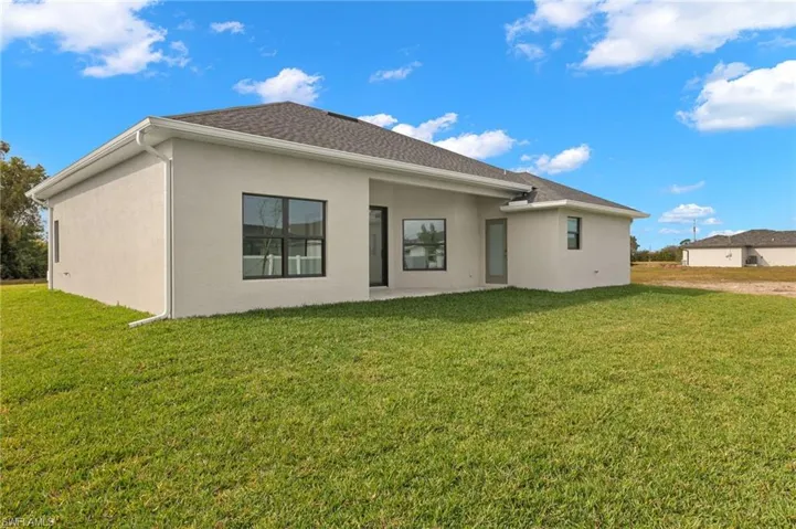 Rear view of property featuring a lawn, stucco siding, and a patio area