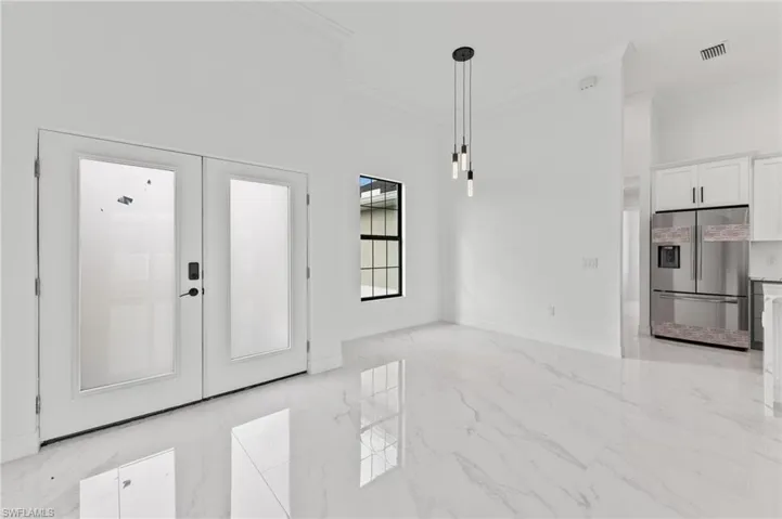 Entrance foyer with ornamental molding, light marble finish flooring, a high ceiling, and french doors