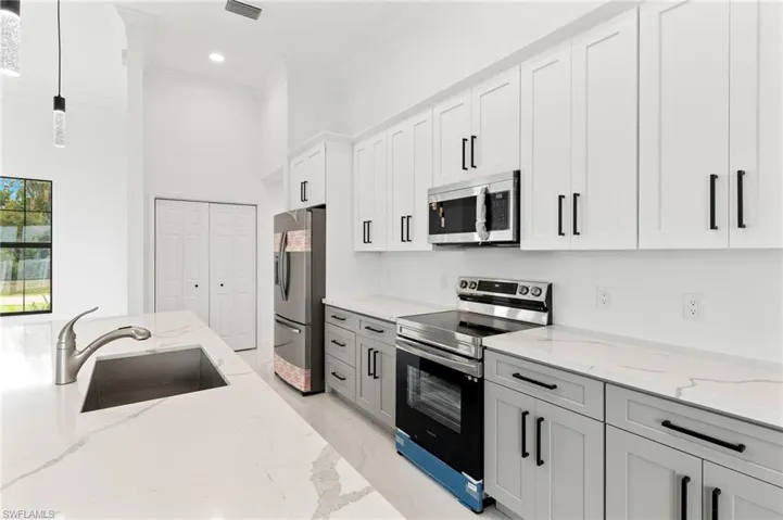 Kitchen featuring stainless steel appliances, light stone counters, a high ceiling, white cabinetry, and decorative light fixtures