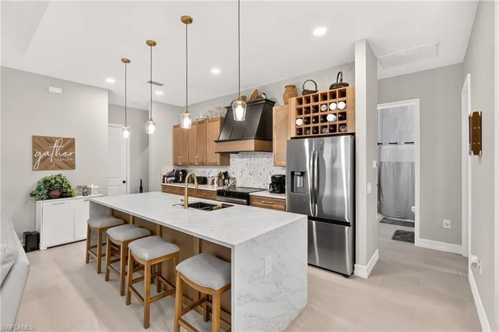 Kitchen featuring a waterfall-edge island with seating, stainless steel appliances, pendant lighting, and light wood-finish cabinetry