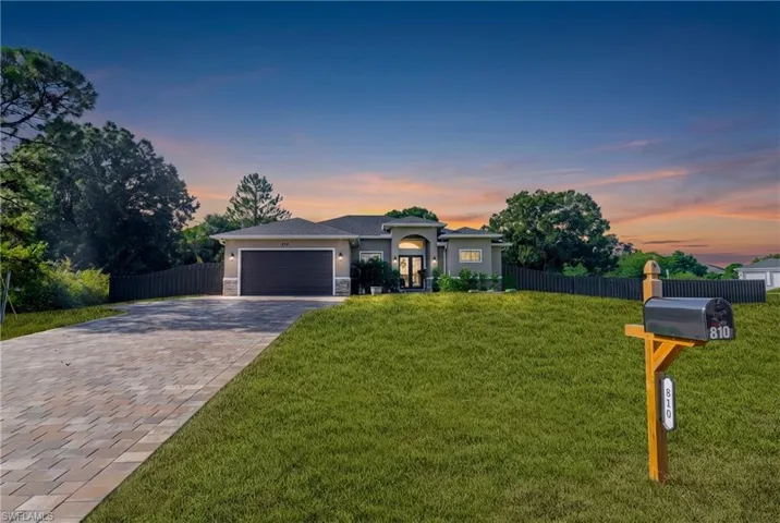 Modern stucco exterior, arched entry, paver driveway, dark garage door, and a privacy fence