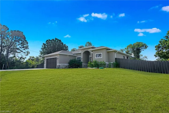 Exterior featuring a two-car garage, stone accent wall, arched entry, and a privacy fence