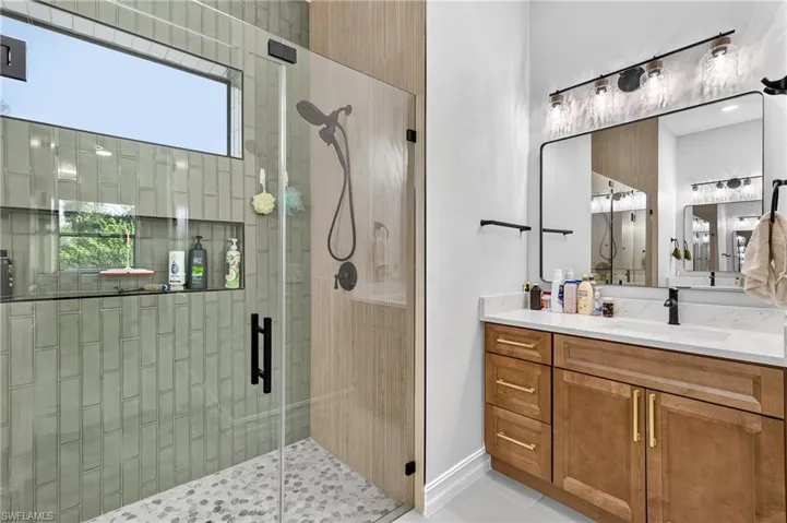 Glass-enclosed shower with vertical subway tile, pebble floor, and built-in niche