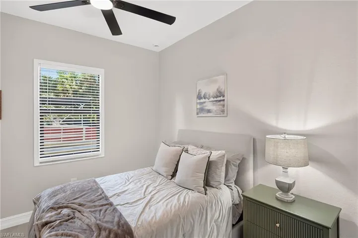 Ceiling fan with integrated lighting, window with blinds, light-colored walls, and textured flooring