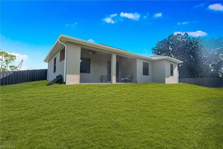 Expansive green lawn with a covered patio featuring a ceiling fan and stucco exterior