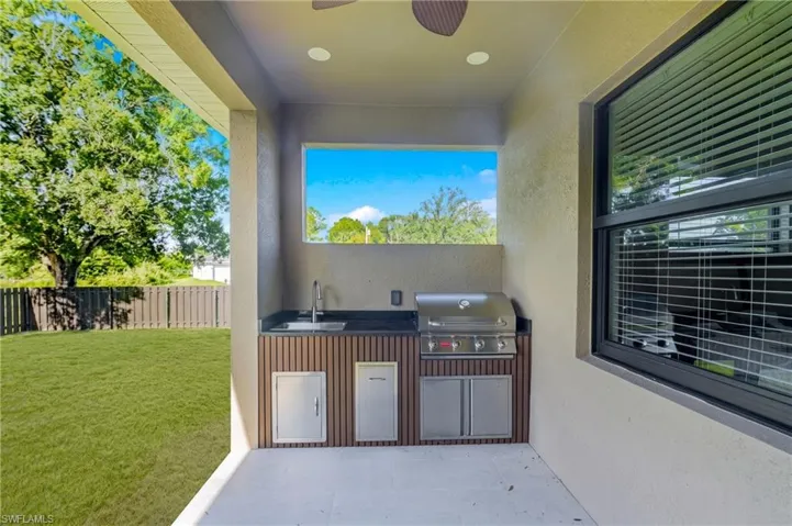 Covered outdoor kitchen featuring a built-in grill, sink, and integrated cabinetry