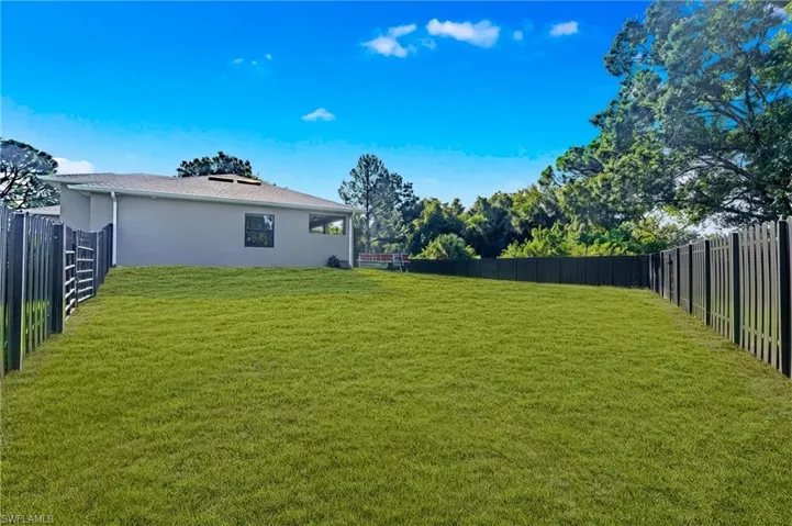 Expansive green lawn with a dark metal fence enclosing the property, featuring a covered patio and a stucco exterior