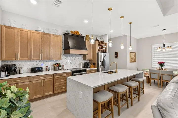 Open-concept kitchen featuring an island with counter seating, stainless steel appliances, custom range hood, and light wood-finish cabinetry