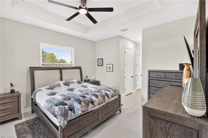 Tray ceiling with a ceiling fan, light gray walls, and wood-finish flooring
