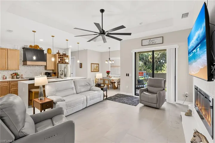 Tray ceiling with a ceiling fan, light-toned tile flooring, kitchen island with seating, pendant lighting, and sliding glass doors to the exterior