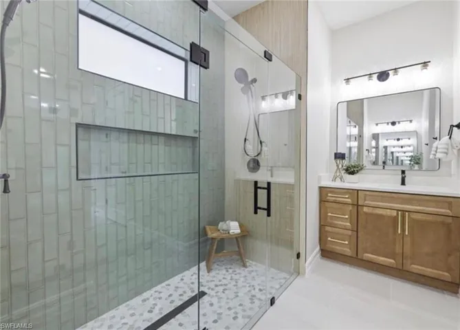 Walk-in shower with vertical subway tile, glass enclosure, and pebble tile flooring