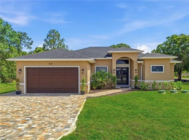 Stucco exterior with stone accents, paver driveway, dark wood-finish garage door, arched entry, and double front doors