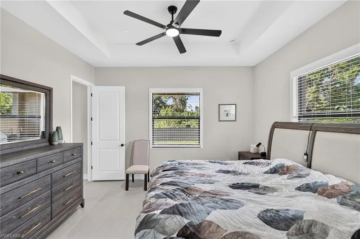 Tray ceiling with a ceiling fan, dual windows with blinds, and light-toned flooring
