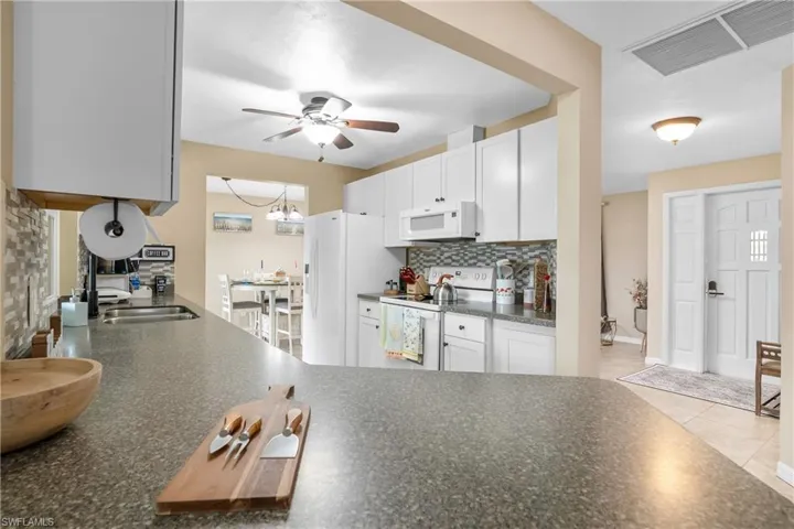 Kitchen with dark countertops, white appliances, white cabinetry, and light tile patterned flooring