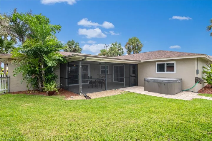 Back of property featuring stucco siding, a lawn, a shingled roof, and a hot tub
