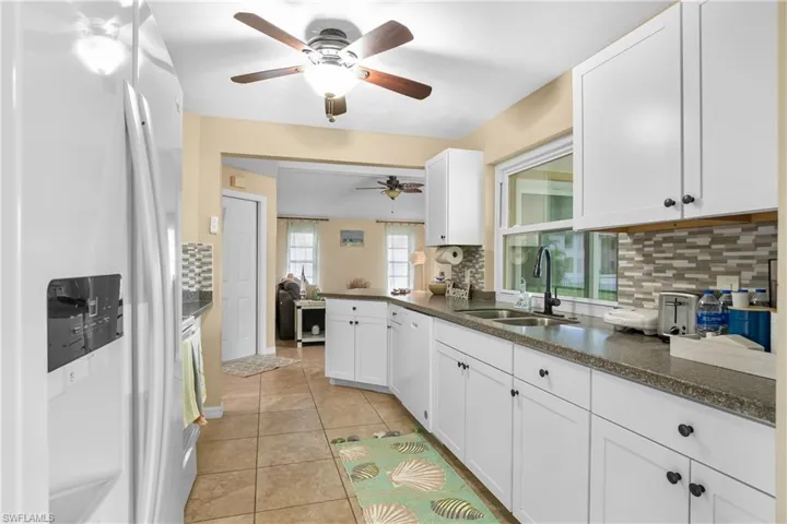 Kitchen featuring white appliances, decorative backsplash, white cabinetry, light tile patterned floors, and a peninsula
