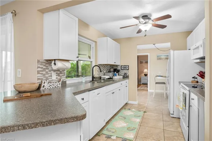Kitchen featuring white appliances, white cabinetry, dark countertops, ceiling fan, and light tile patterned floors