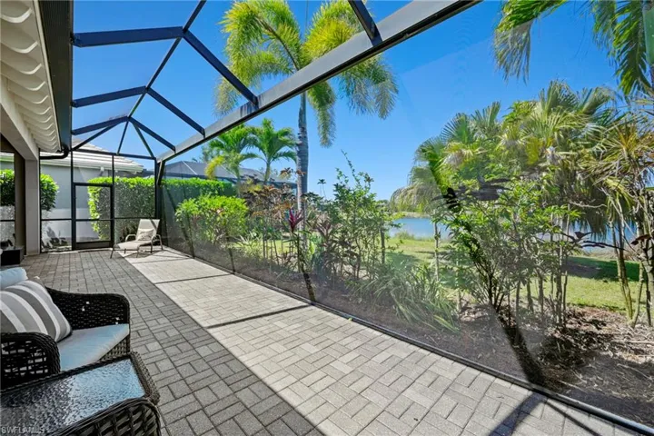 Screened lanai featuring paver flooring, direct water frontage, and lush landscaping