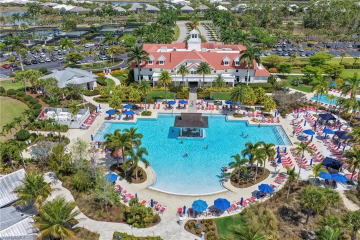 Expansive aquatic amenity featuring a large swimming pool with an in-pool structure, multiple lounge areas with umbrellas, and a surrounding paved deck