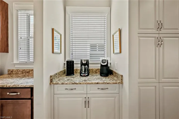 Kitchenette area featuring light-toned countertops, white shaker-style cabinetry, and integrated windows with blinds