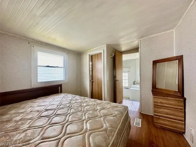 Unfurnished bedroom with wood-type flooring, ensuite bathroom, and lofted ceiling