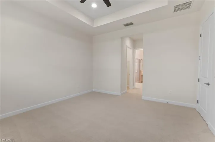 Primary Bedroom with new carpet featuring a tray ceiling and ceiling fan