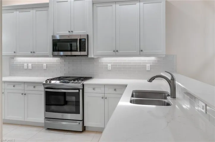 Kitchen featuring white cabinets, light tile patterned flooring, sink, appliances with stainless steel finishes, and decorative backsplash