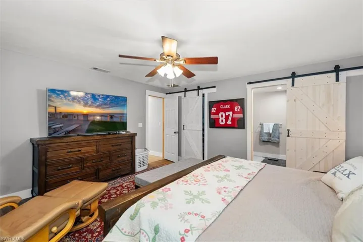 Bedroom with a barn door, ensuite bathroom, and a ceiling fan