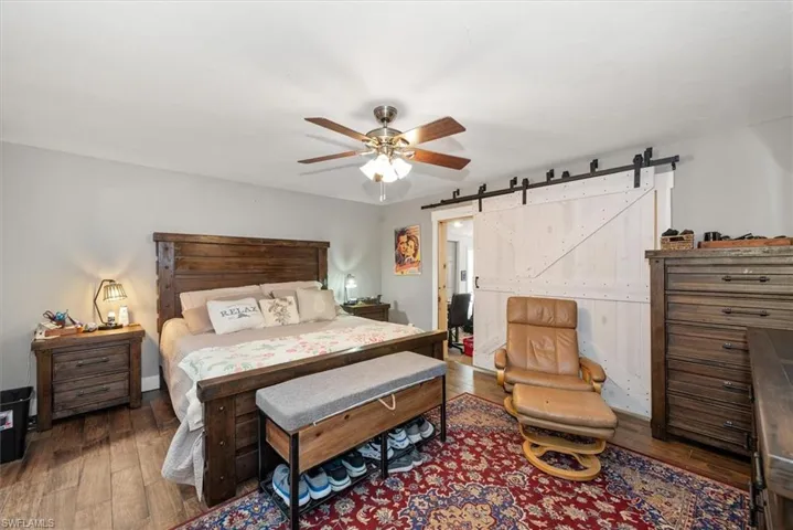 Bedroom featuring a barn door, dark wood-style flooring, and a ceiling fan