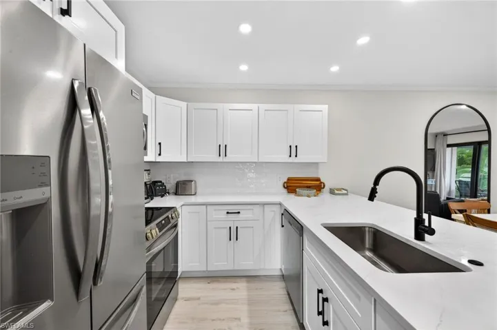 Kitchen featuring stainless steel appliances, light stone counters, white cabinets, crown molding, and light wood-style floors