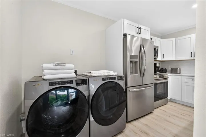 Laundry area featuring ornamental molding, independent washer and dryer, and light wood-style floors