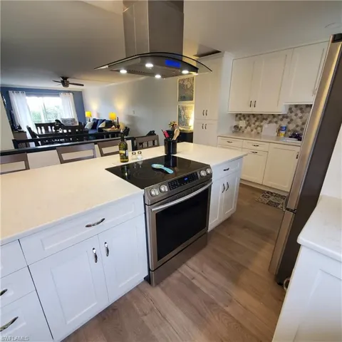 Kitchen with white cabinetry, island exhaust hood, appliances with stainless steel finishes, and light stone counters