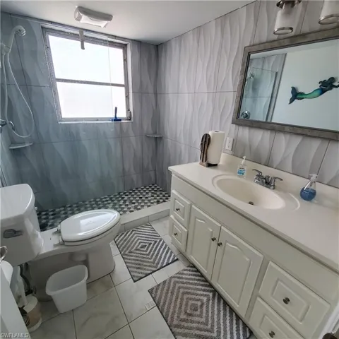 Bathroom with a stall shower, vanity, tile walls, and light tile patterned flooring