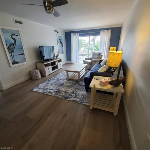 Living room with dark wood finished floors, crown molding, and ceiling fan