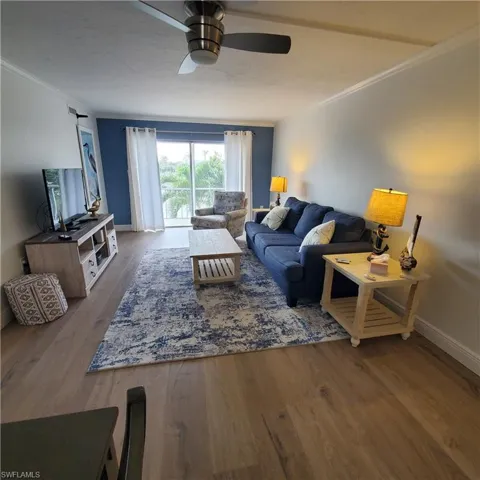 Living area with crown molding, dark wood finished floors, and a ceiling fan