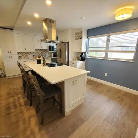 Kitchen with tasteful backsplash, white cabinetry, an island with sink, island exhaust hood, and stainless steel appliances