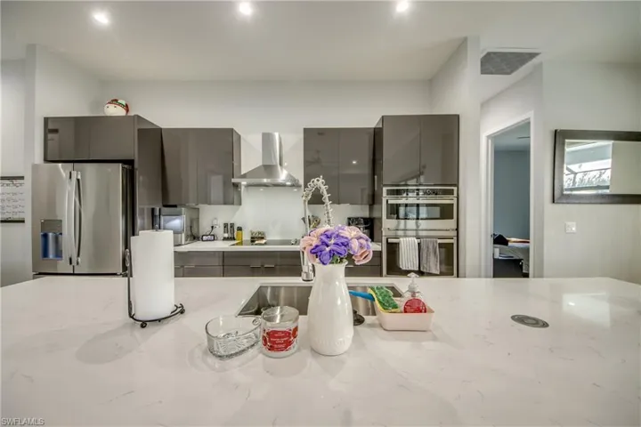 Kitchen with stainless steel appliances, modern cabinets, wall chimney range hood, gray cabinetry, and light stone countertops