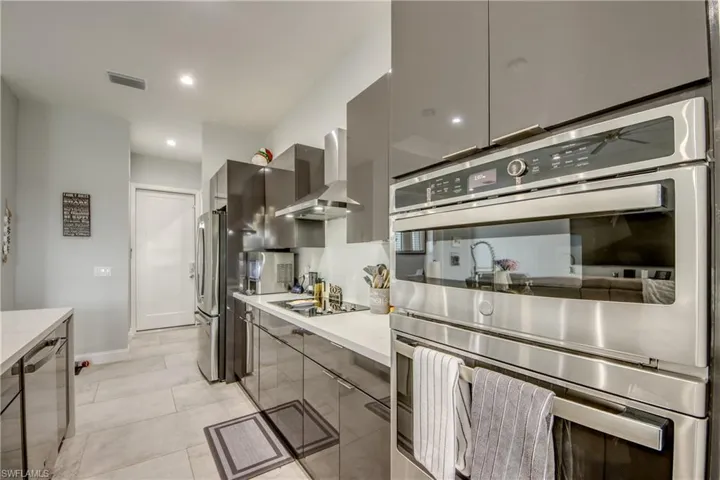 Kitchen with appliances with stainless steel finishes, wall chimney exhaust hood, modern cabinets, recessed lighting, and gray cabinetry