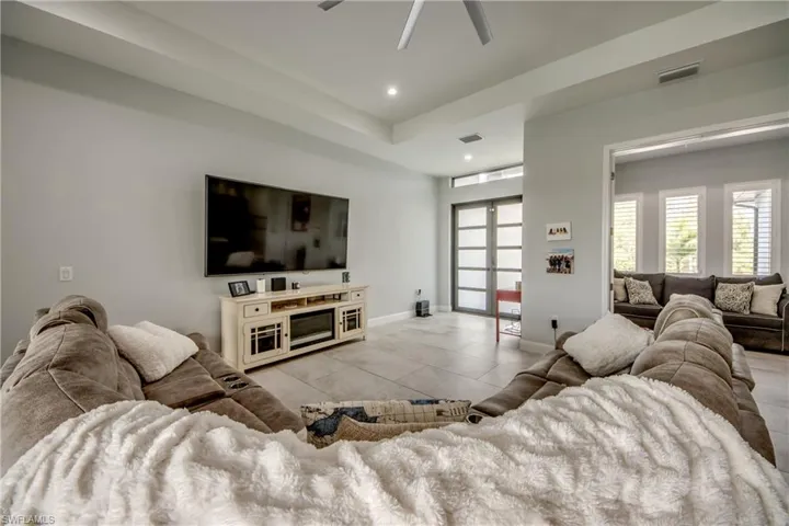 Living room with a raised ceiling, recessed lighting, and a ceiling fan