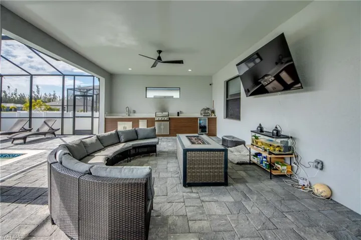 View of patio with an outdoor kitchen, an outdoor living space with a fire pit, a sunroom, a lanai, and a ceiling fan