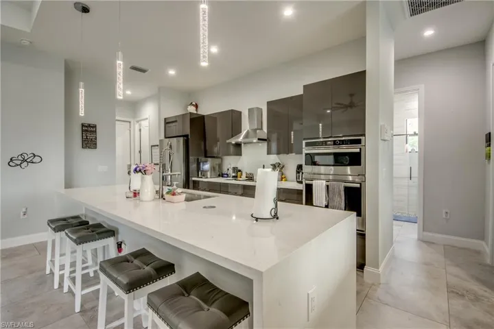 Kitchen with hanging light fixtures, a breakfast bar area, a large island with sink, wall chimney range hood, and stainless steel appliances