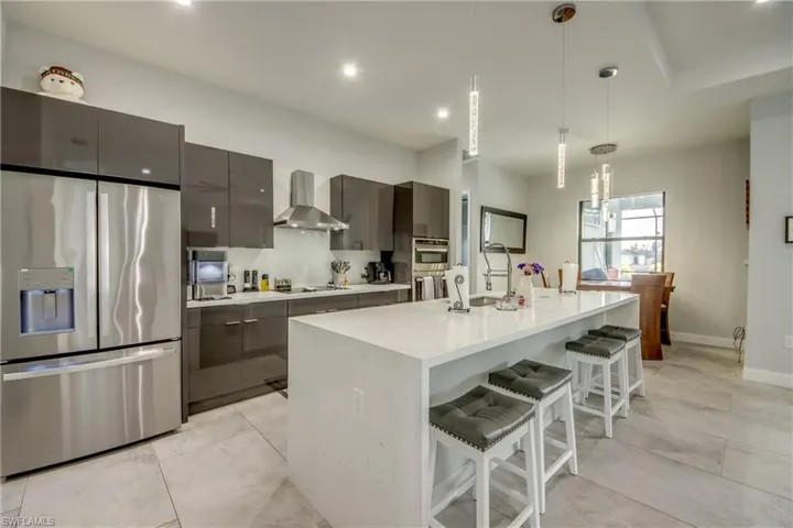 Kitchen featuring stainless steel refrigerator with ice dispenser, a breakfast bar, hanging light fixtures, a center island, and wall chimney range hood