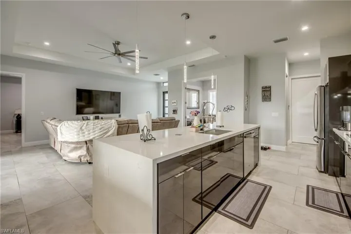 Kitchen featuring hanging light fixtures, a ceiling fan, a tray ceiling, appliances with stainless steel finishes, and light stone countertops