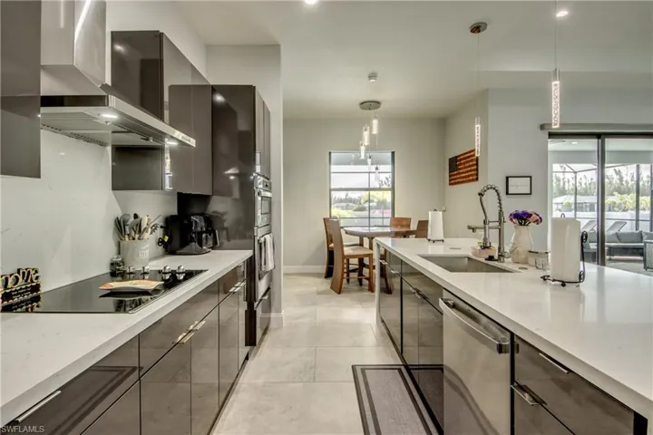 Kitchen featuring hanging light fixtures, modern cabinets, wall chimney exhaust hood, light stone countertops, and recessed lighting